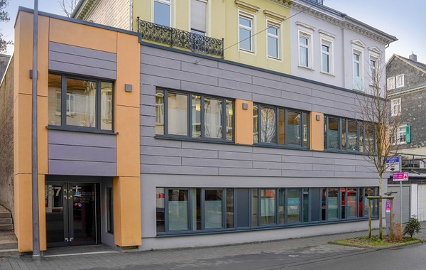 Modernes Bürogebäude mit großen Fenstern und bunter Fassade in einer Innenstadt.