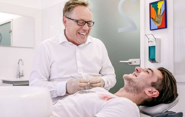 Zahnarzt behandelt lachenden Patienten in moderner Praxis für professionelle Zahnmedizin.