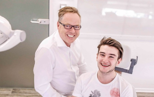 Zahnarzt und junger Patient lächeln gemeinsam in moderner Zahnarztpraxis.