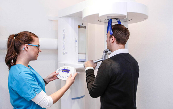 Zahnärztin führt mit digitalem Röntgengerät eine moderne Panoramaaufnahme beim Patienten durch.
