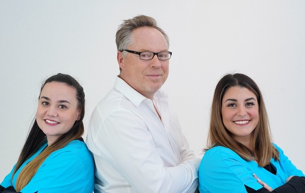 Drei freundliche Zahnärzte im Team vor weißem Hintergrund, lächeln in die Kamera.