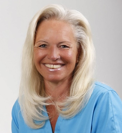 Porträt einer lächelnden älteren Frau mit langen blonden Haaren in blauer Kleidung.